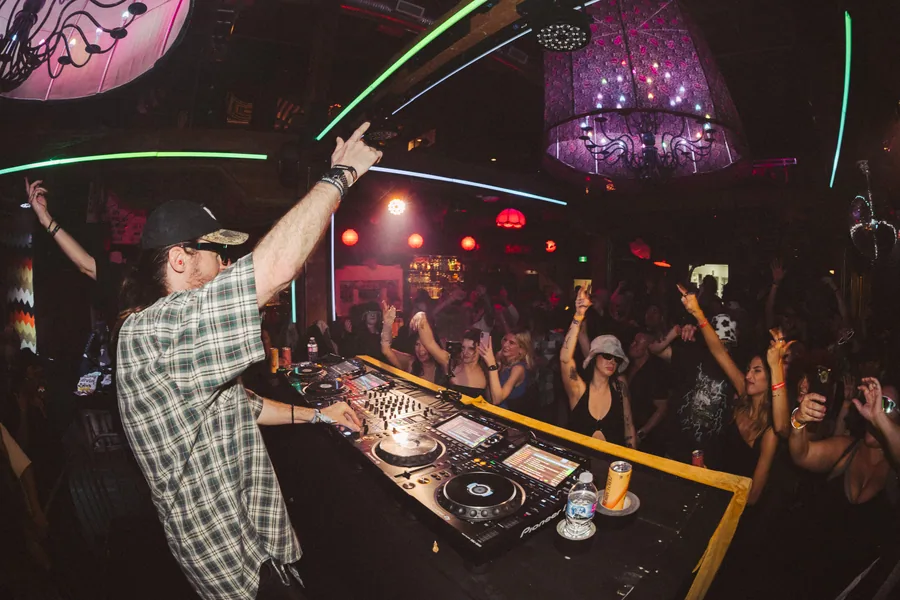 DJ with an arm up over a packed floor under lasers