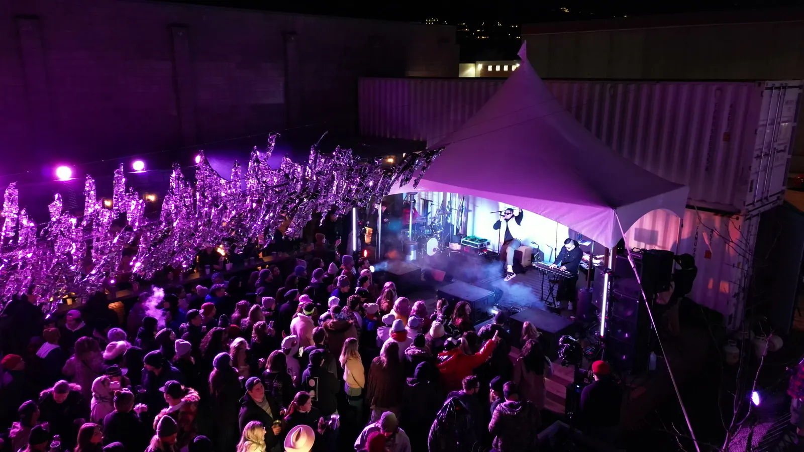 A crowd in front of the stage tent under purple light