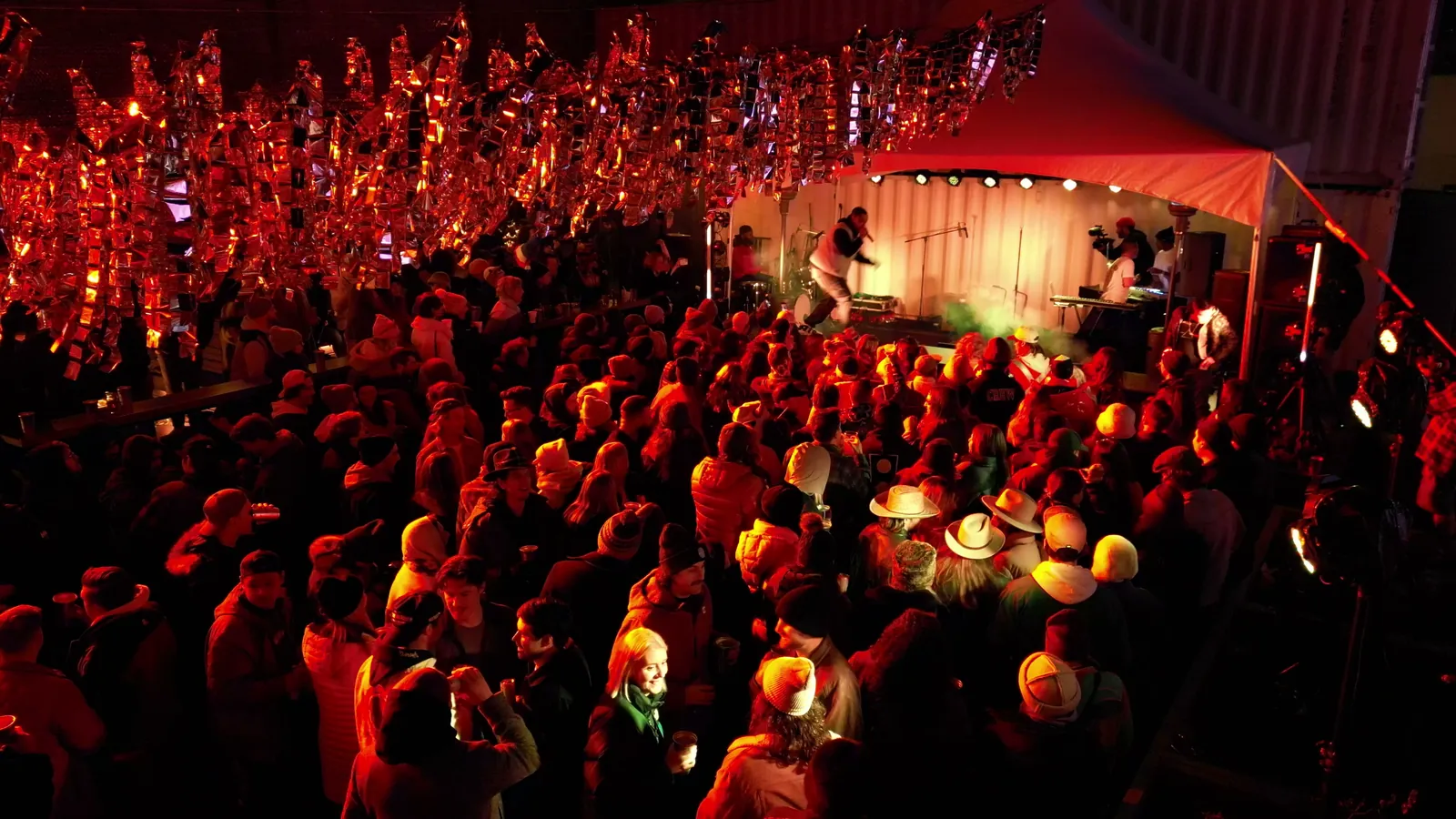 A packed outdoor crowd under red tinsel, from the drone